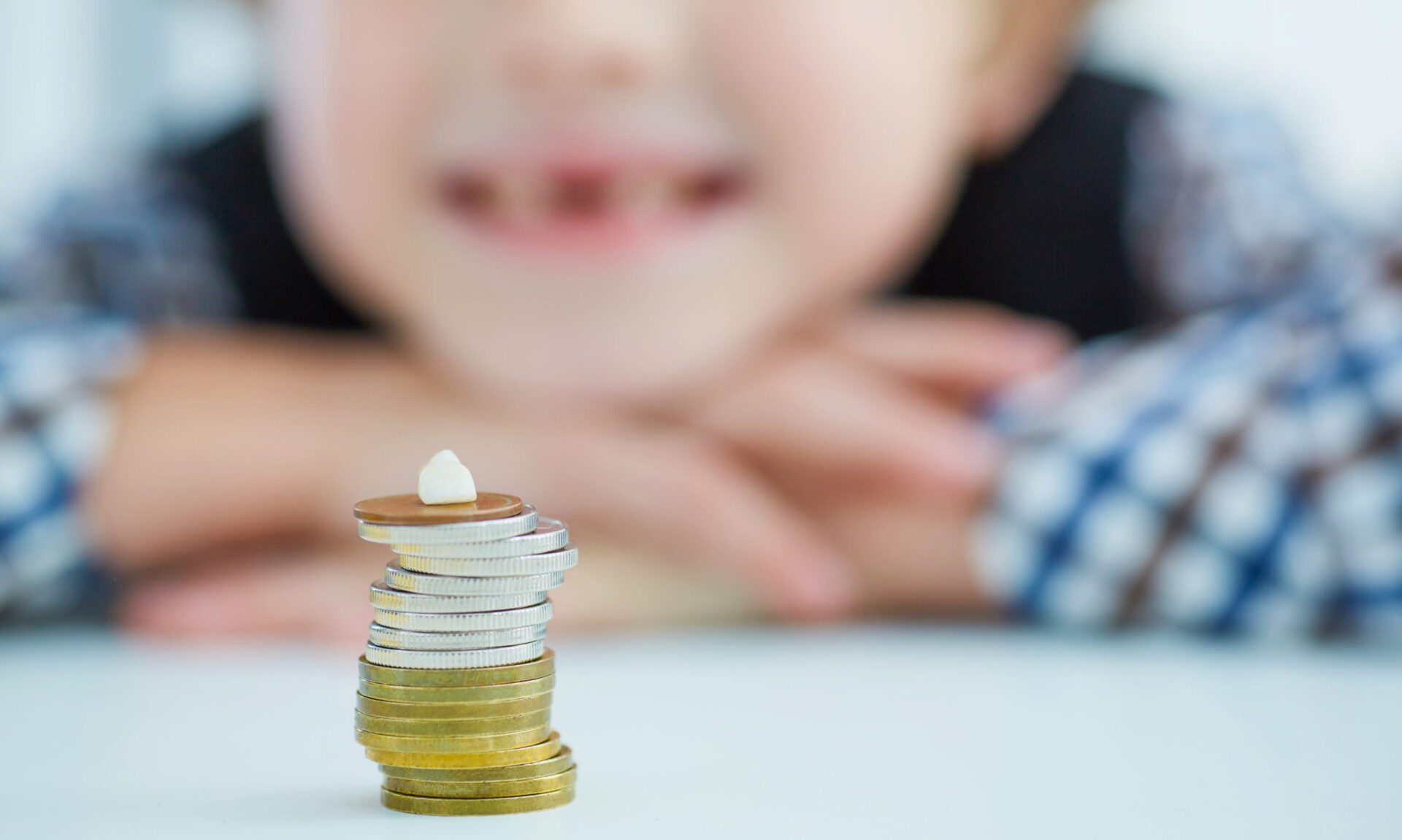 Smiling young boy with missing front tooth. Pile of coins with a baby tooth on top. Tooth fairy giving money coins as a reward for child teeth.