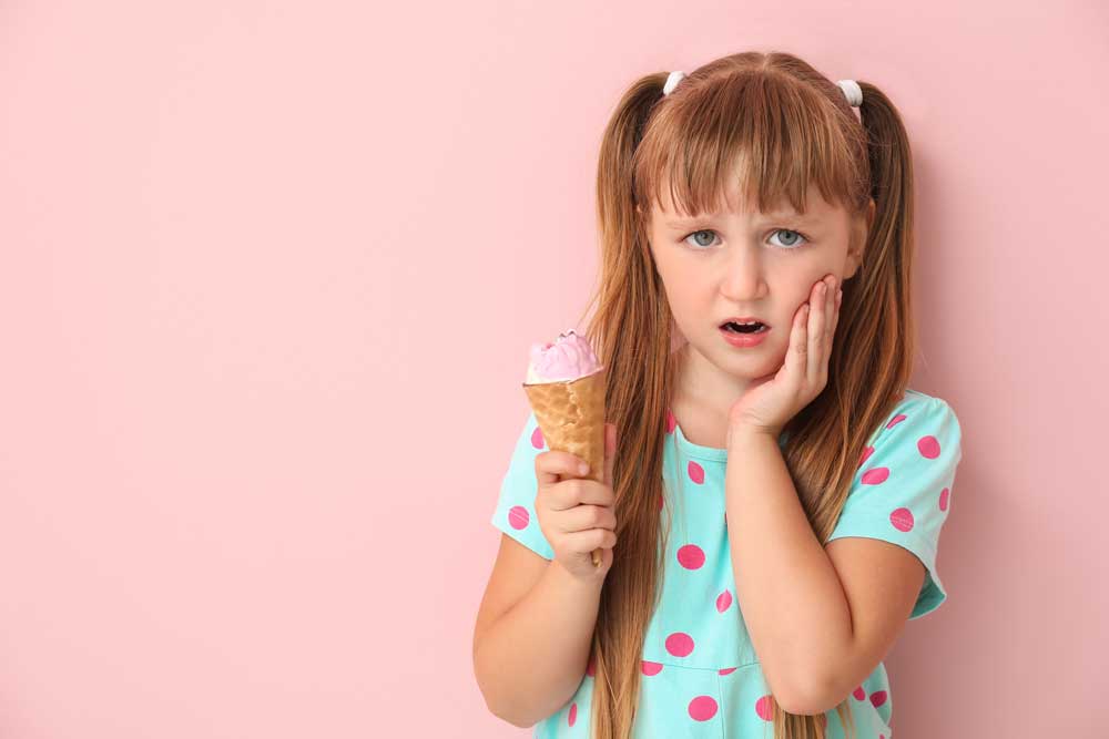 young girl experiencing tooth sensitivity after eating ice cream