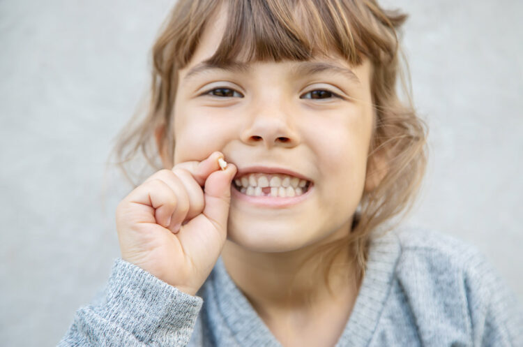 young girl holding lost tooth in hand