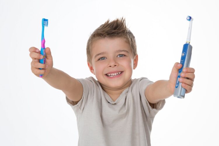 boy holds up an electric toothbrush and a regular toothbrush