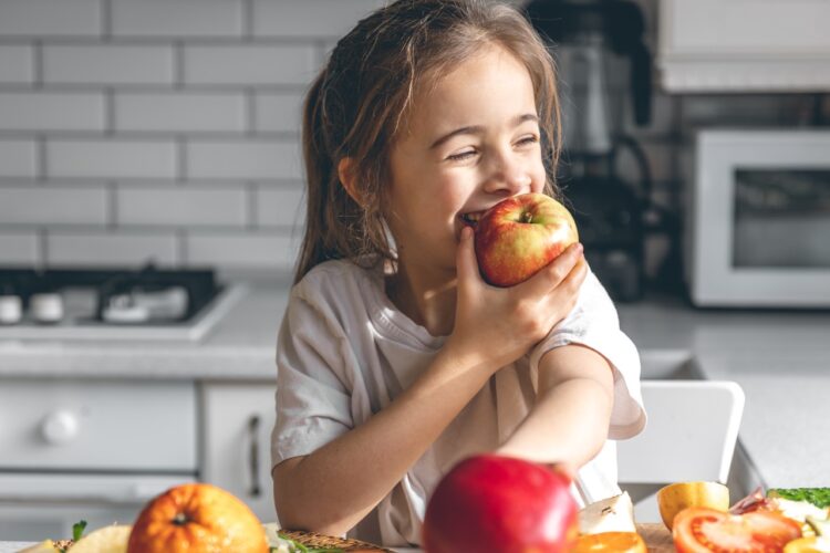 little girl bites into apple with teeth